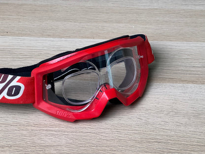 Red 100% goggle on wooden surface, front view with prescription insert visible through clear lens