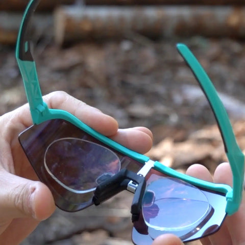 Hands holding teal Oakley Sutro Lite Sweep from inside showing prescription clip insert installed