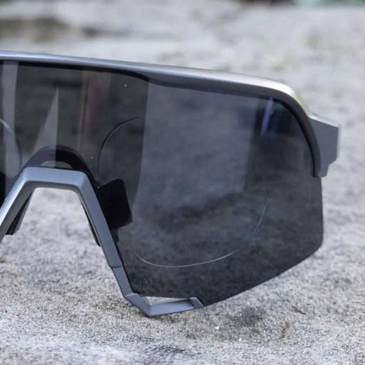 Shield-style sport sunglasses with prescription insert visible through dark lens, on granite surface